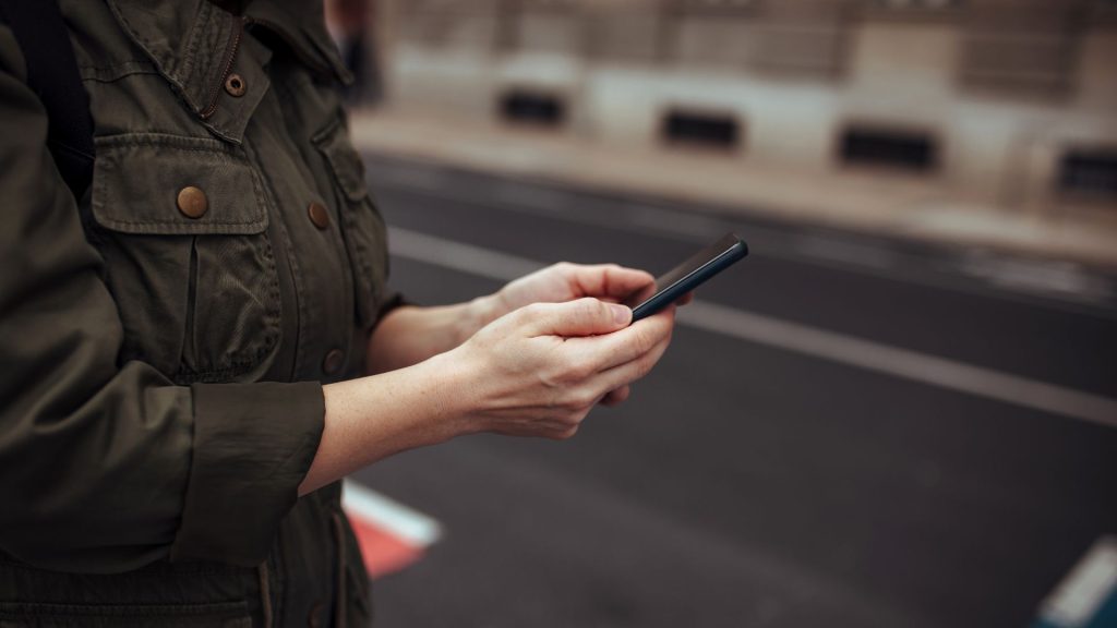 Person using a smartphone while waiting on a city street